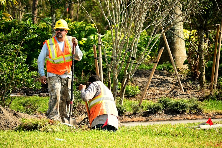 Two Male Construction Workers Digging In Soil