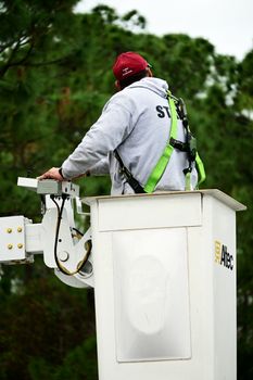 A worker wearing safety gear operates a bucket truck, focusing on safety and equipment handling.