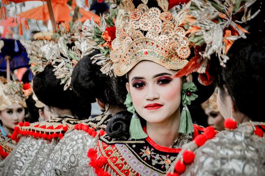 Colorful traditional parade with women in ornate headdresses and makeup, celebrating cultural heritage.