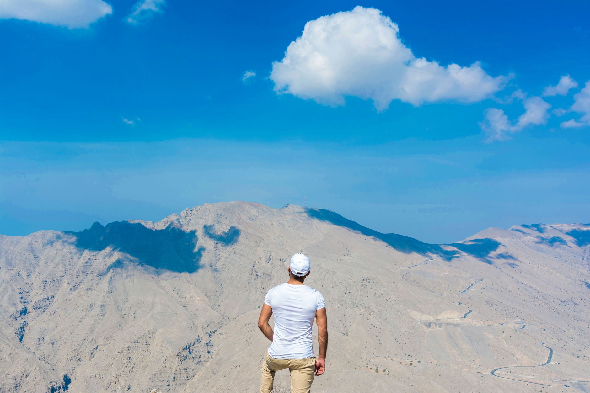 Man stands admiring vast Hajar Mountains in Ras al Khaimah, UAE under a clear blue sky. โ photo by San Photography / Pexels
