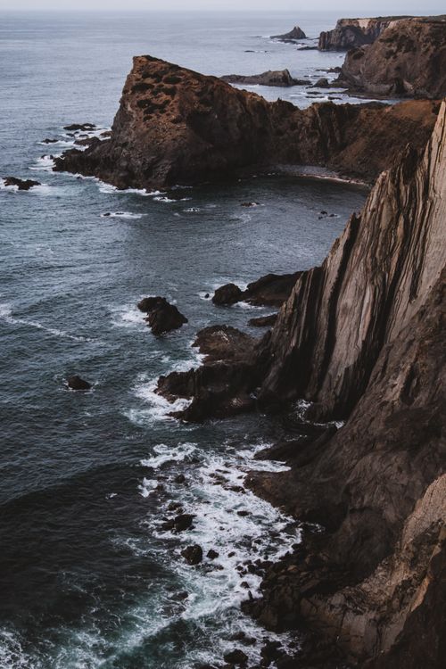 Free Stunning aerial view of craggy coastal cliffs with waves crashing below at twilight. Stock Photo