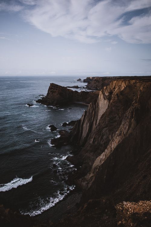 Free Stunning view of rugged coastal cliffs meeting the ocean under a dramatic sky at sunset. Stock Photo