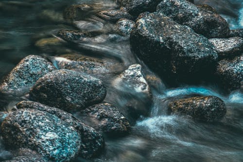 Scenic view of shallow river with rapid water fluid between big stones with spots in daylight