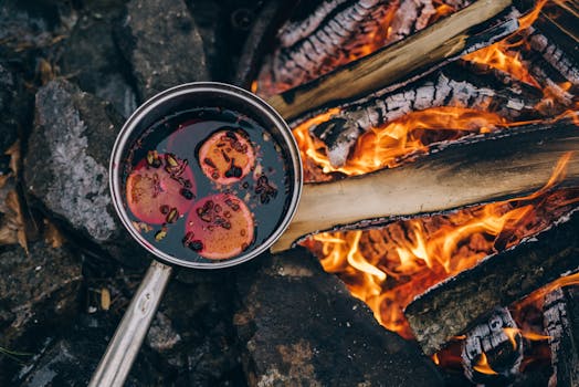 A pot of mulled wine simmering over a campfire, surrounded by natural stones and flames.