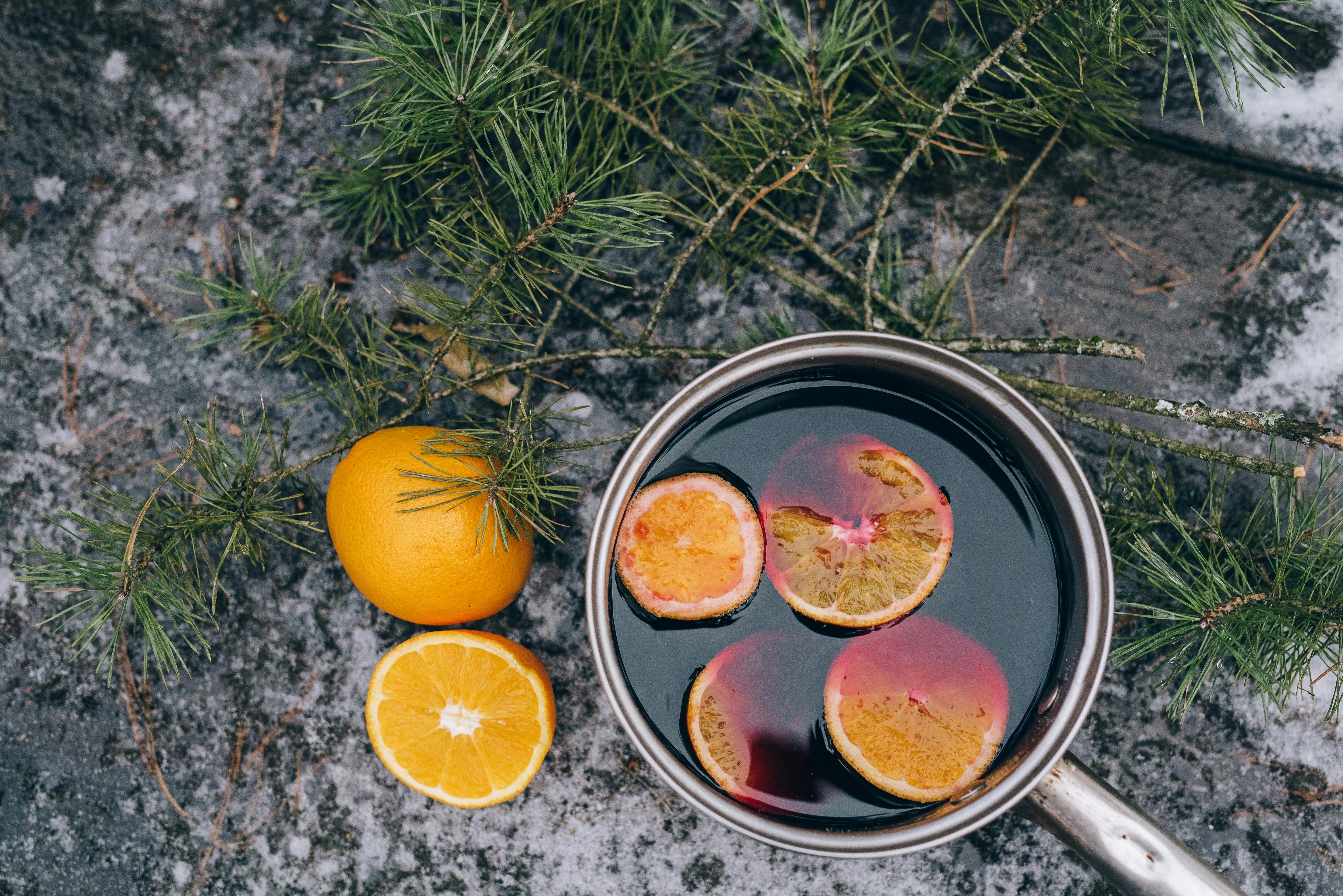 Hot wine drink simmering in a steel saucepan with fresh orange slices and pine branches - winter mulled wine recipe in progress