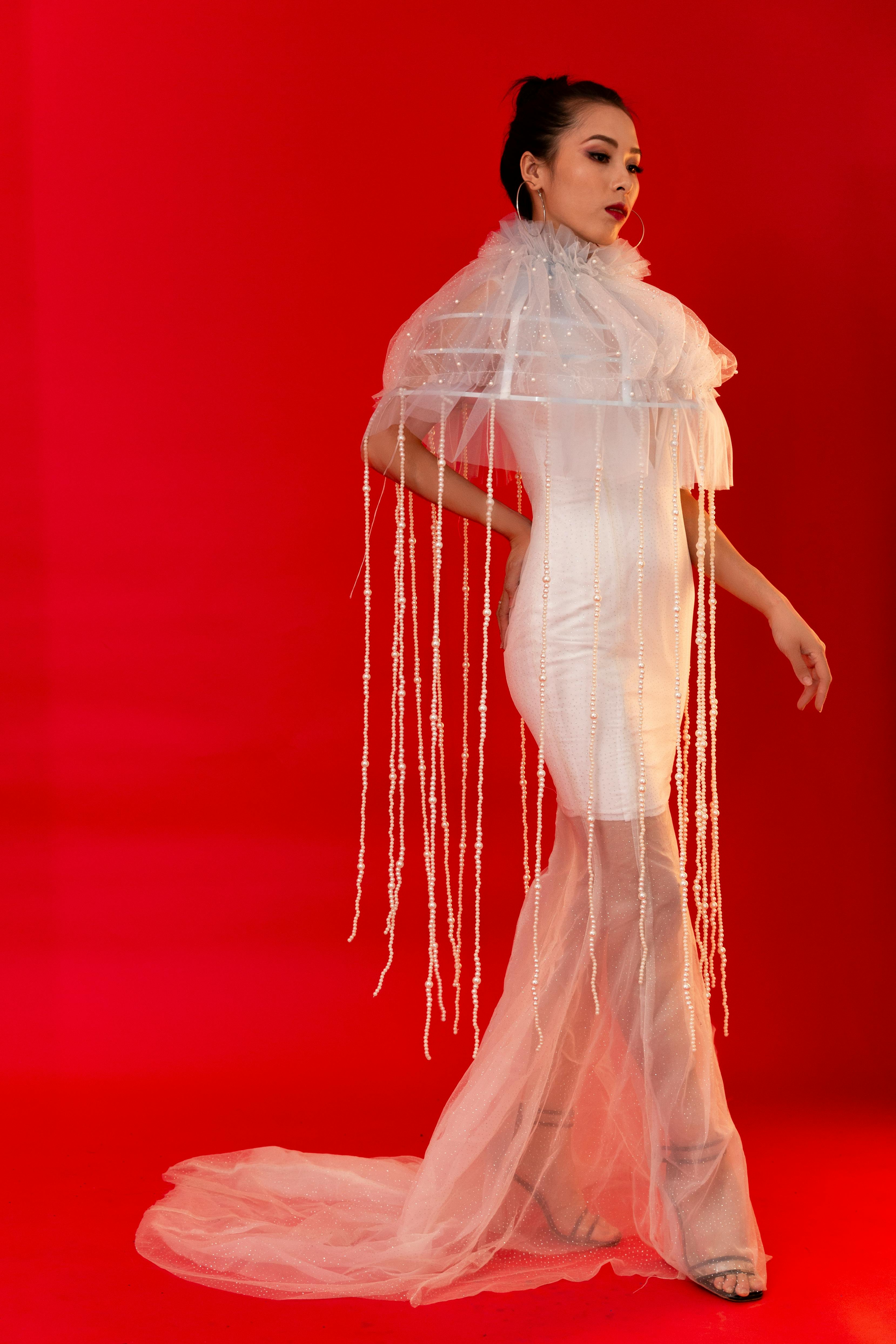 Fashionable woman posing elegantly in a white dress with a striking red background.