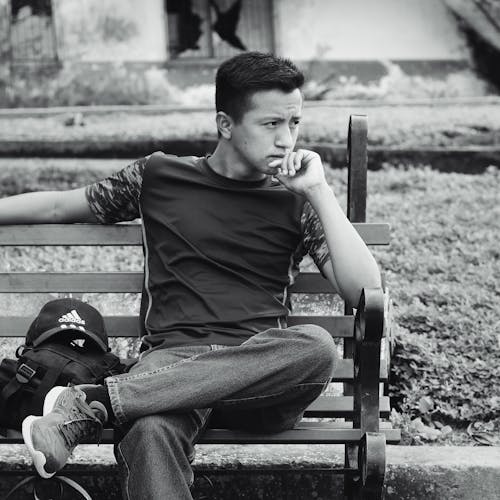A Grayscale of a Man Sitting on a Bench