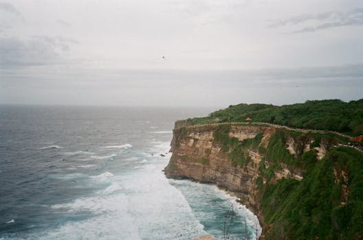 Breathtaking view of waves crashing against green cliffs under a moody sky.