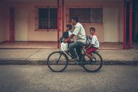 Father and sons ride a bike through a Cuban street, showcasing family togetherness and local culture.