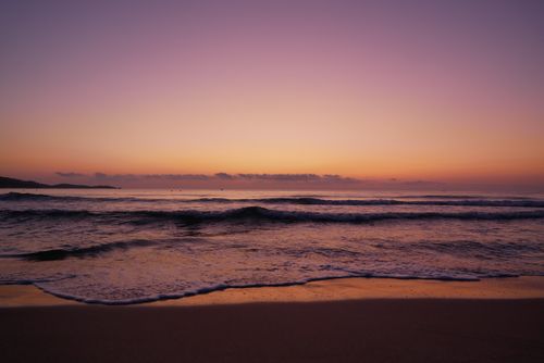 Free A serene beach scene at sunset with soft waves and a vibrant sky reflecting on the water. Stock Photo