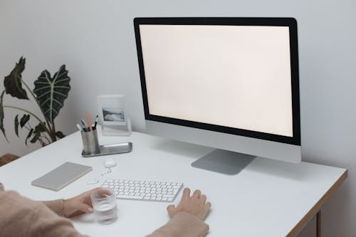 Crop anonymous person in sweater sitting at table with glass of water while working at computer