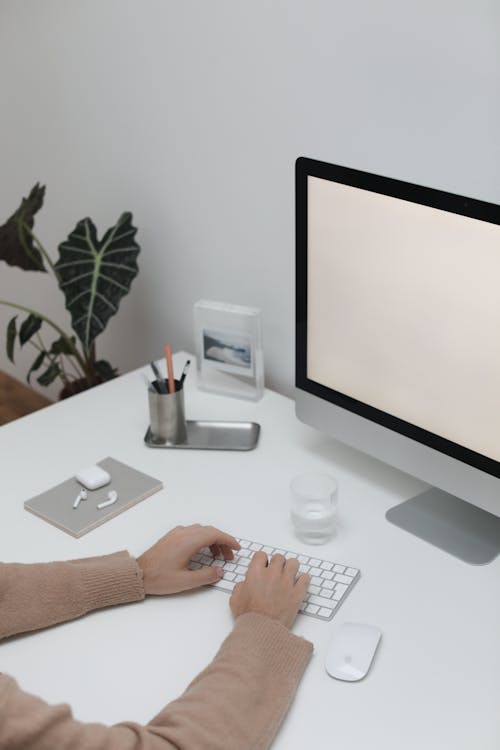 High angle of crop unrecognizable person typing on computer keyboard while sitting at table with wireless keyboard