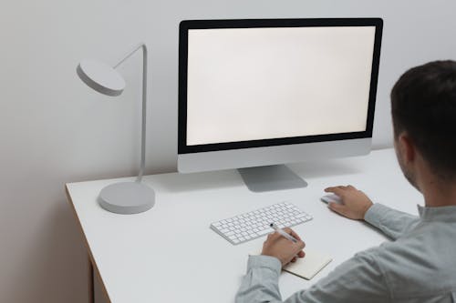 Free Crop anonymous male worker in formal clothes taking notes while browsing computer in modern workplace Stock Photo