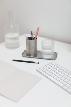 Workspace with opened notebook near pencil and glass with water near wireless keyboard