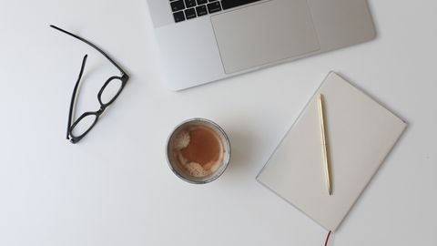 Escritorio visto desde arriba con portátil, gafas, taza y cuaderno