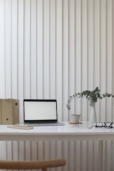 Contemporary workplace with netbook near plant in vase and cardboard folders on table