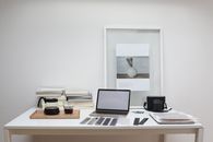 Modern laptop with blank screen arranged with retro filmstrips photo camera and framed picture placed on table near coffee and stack of books