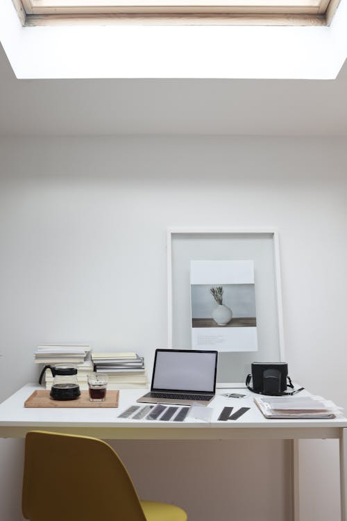 Netbook with white screen and retro camera placed on table with filmstrips and coffee glass during printing photos in office