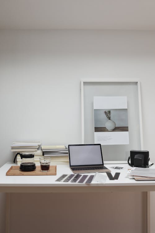 Photographer working desk with modern laptop and filmstrips scattered near film camera and glass of coffee decorated with framed picture