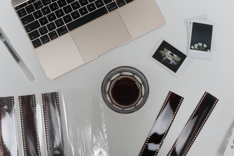 Laptop With Instant Photos And Film Strips Placed On Desk Near Aromatic Coffee