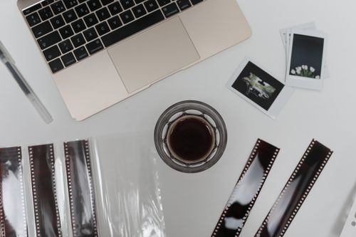 Free Top view of coffee cup with vintage instant photos and negative film strips placed on table with opened laptop Stock Photo
