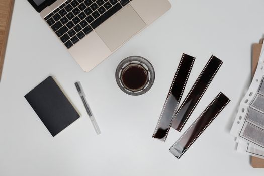 Top view of filmstrips with coffee cup and notebook placed on working desk with opened laptop