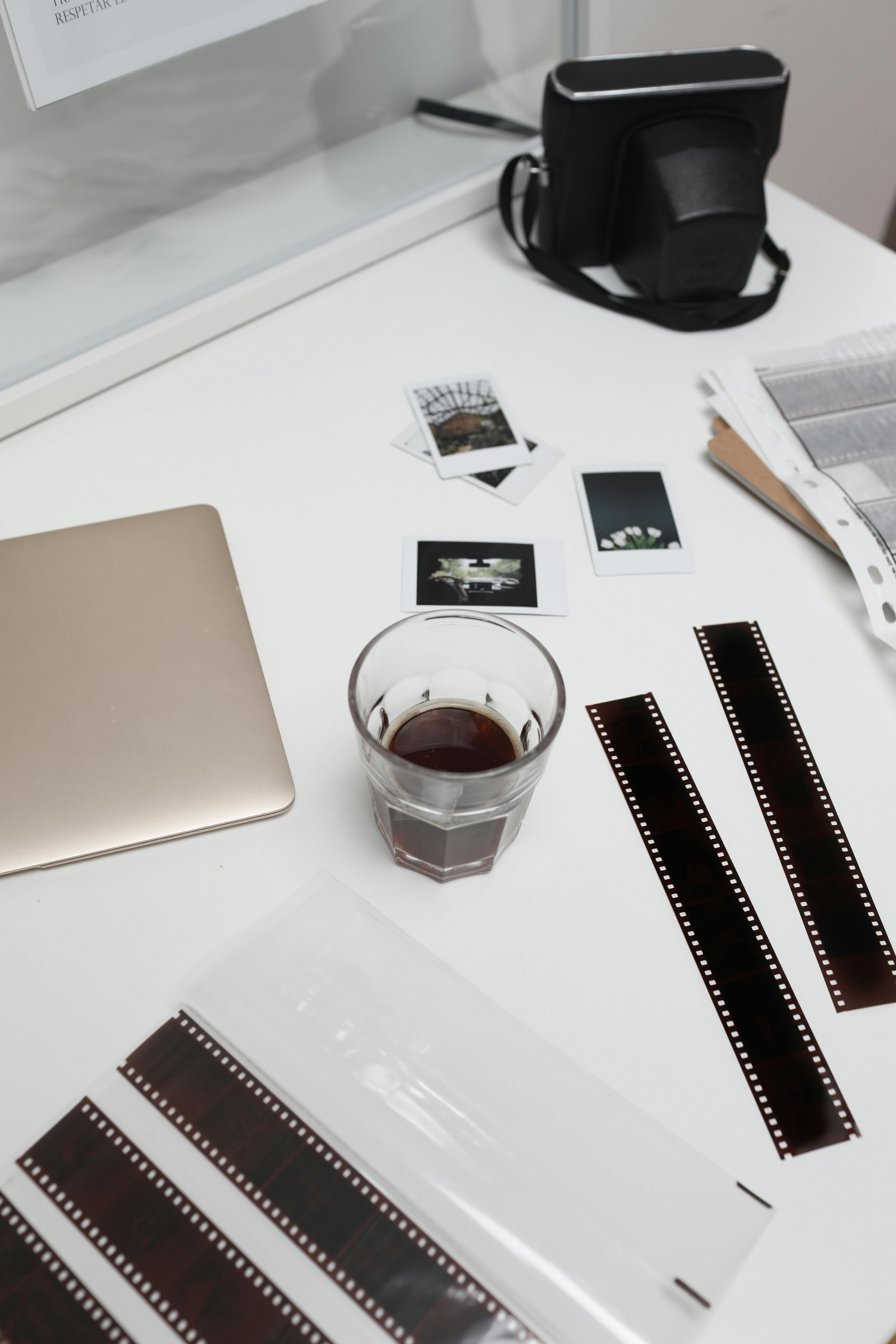 coffee glass on table with laptop and retro camera near filmstrips and photos