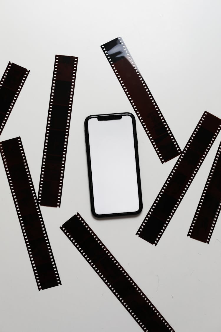 Film Tapes Scattered On Table Near Smartphone