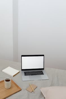 A clean, minimalist workspace featuring an open laptop, coffee cup, notebook, and pencil on a tidy desk.