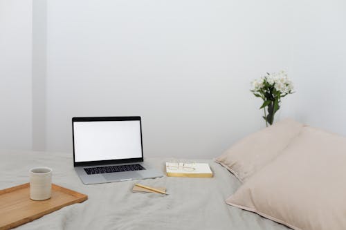 Laptop and book placed on soft bed with coffee cup during remote studies