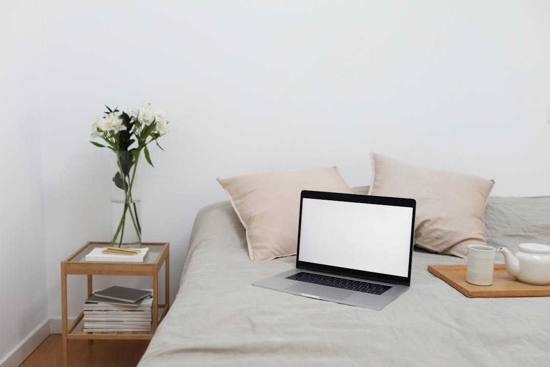 Free Tray with tea set and laptop placed on bed near table with flowers vase Stock Photo