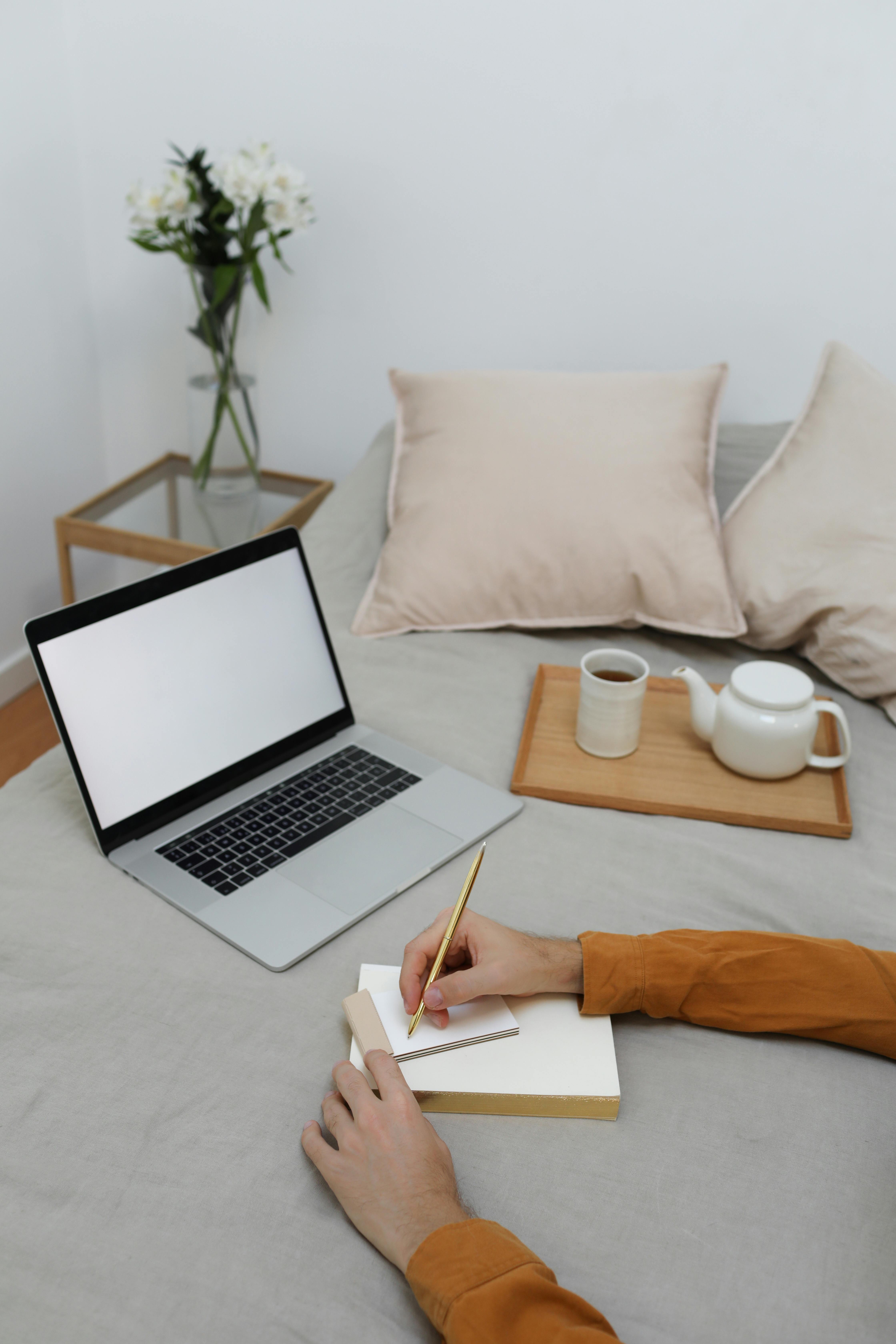 anonymous man taking notes while working on laptop in bedroom