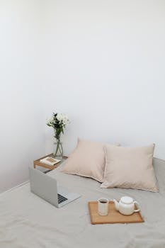 Minimalist bedroom setup with a laptop, coffee, and flowers, ideal for telecommuting.