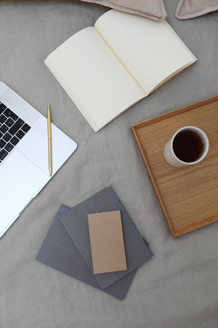 Opened Notebook And Laptop Placed Near Wooden Tray With Coffee Cup On Bed