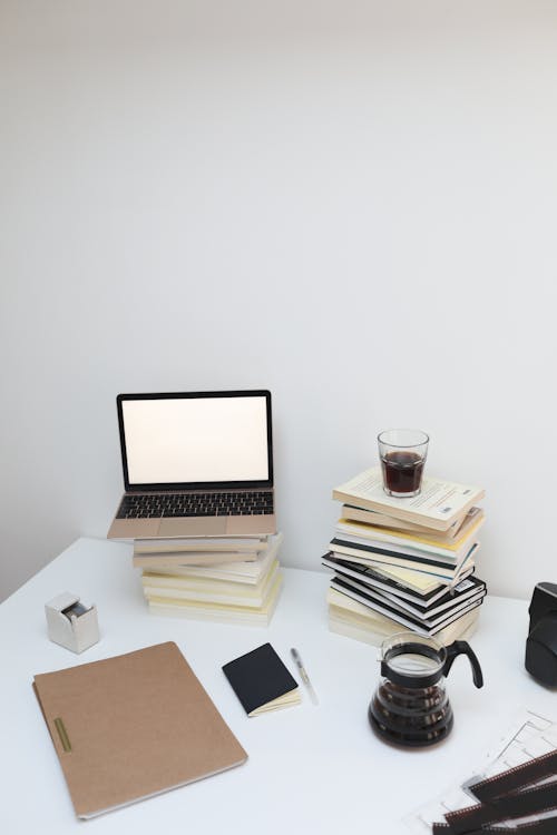 Opened laptop with empty screen placed on stack of books placed on white table against white wall in light room