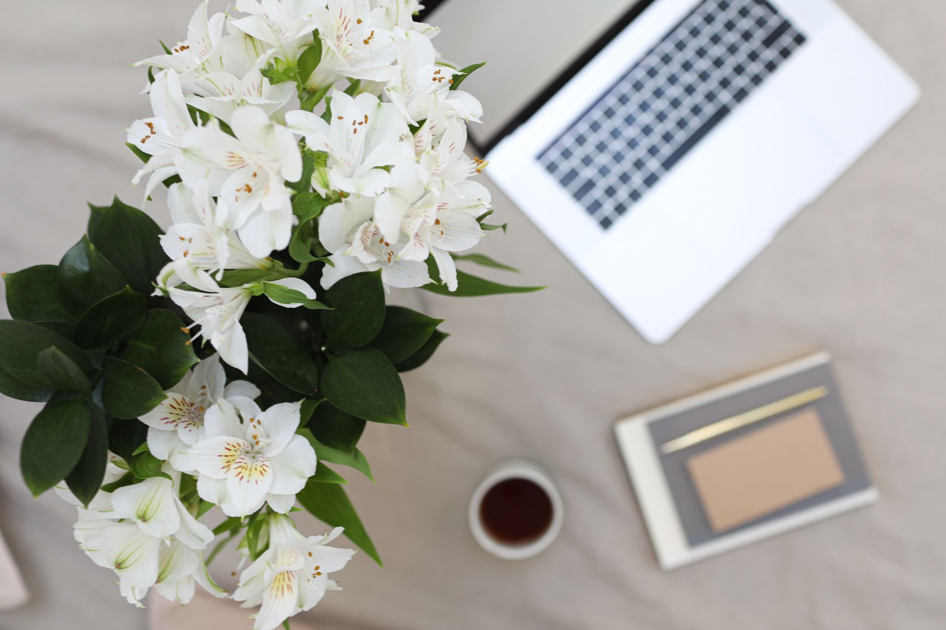 From above of bouquet of fresh lilies places near opened laptop and notebook with pen on fabric surface in daytime