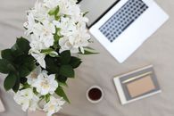 From above of bouquet of fresh lilies places near opened laptop and notebook with pen on fabric surface in daytime
