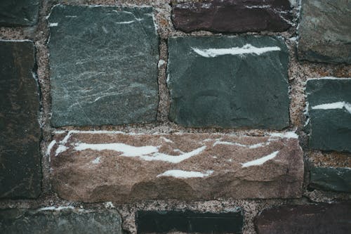 Textured surface of rough stone wall with cracks and snow as abstract background