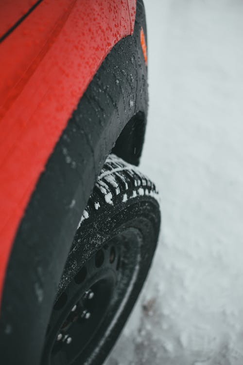 From above of wheel of modern red car parked on snowy road on winter day