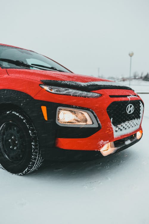 Modern red and black off road car with glowing headlights parked in road covered with snow under foggy gray sky in winter