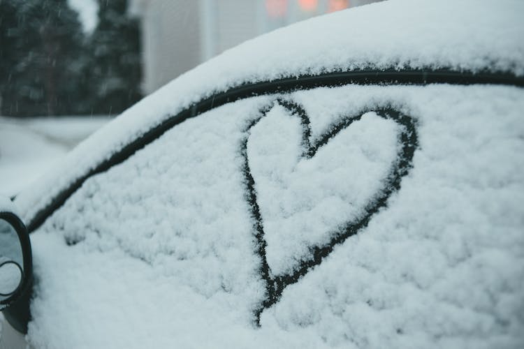 Heart On Snowy Window Of Car Parked On Street In Winter