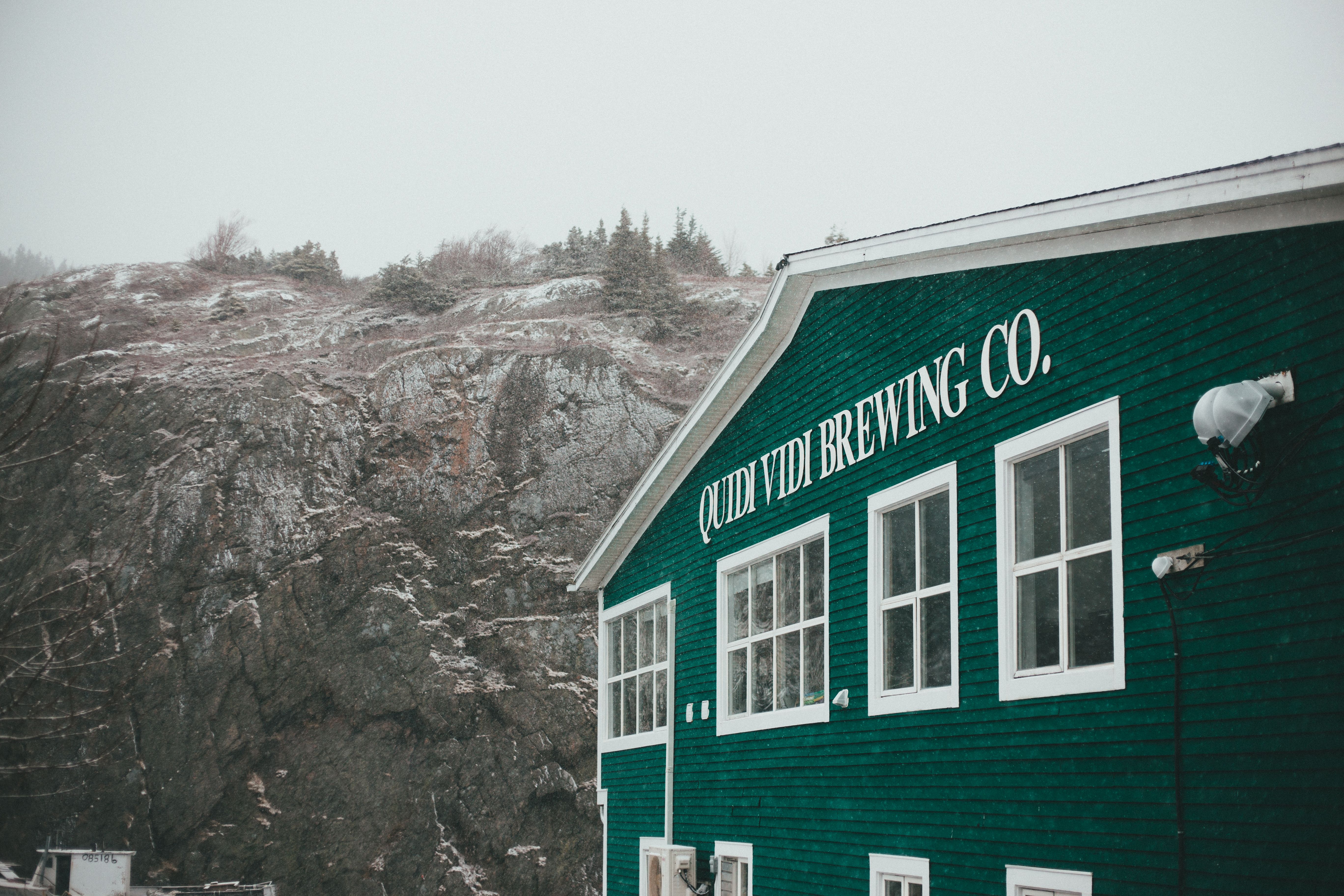 Snow-dusted Quidi Vidi Brewing Co. set against a rugged rock formation in Newfoundland's winter landscape.