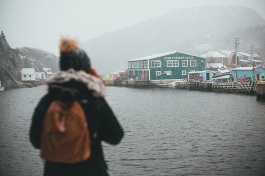 A tourist admiring the snowy landscape at Quidi Vidi Village with iconic brewery in sight.