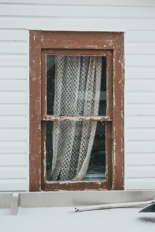 Old rustic wooden house with shabby window frame covered with curtain in countryside