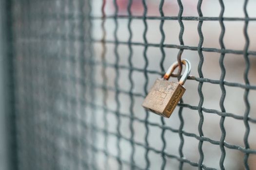 Small iron lock hanging on rusty metal grid for protection and safety of private area