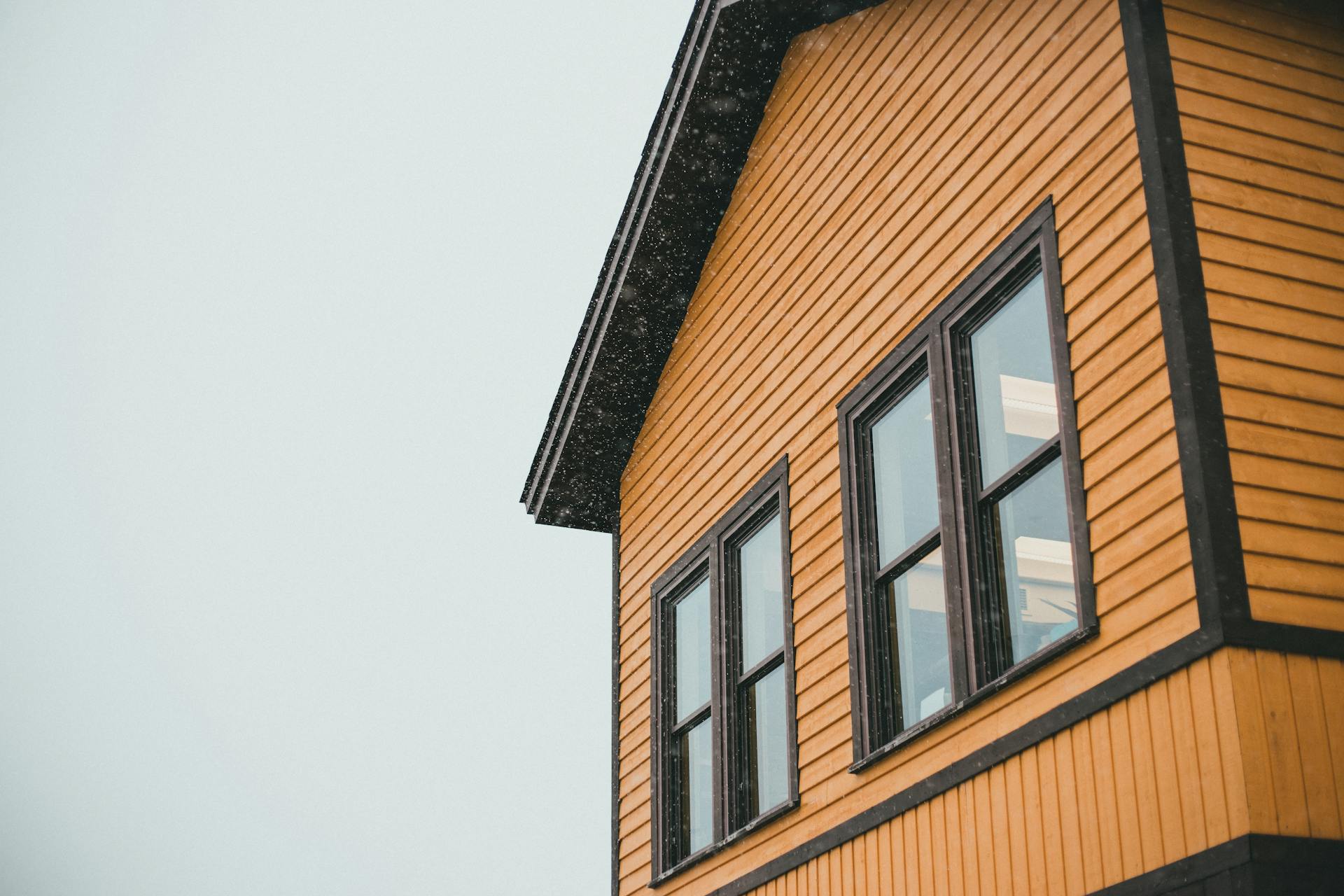 Close-up of a yellow wooden house with black trim and falling snow, creating a wintery feel.