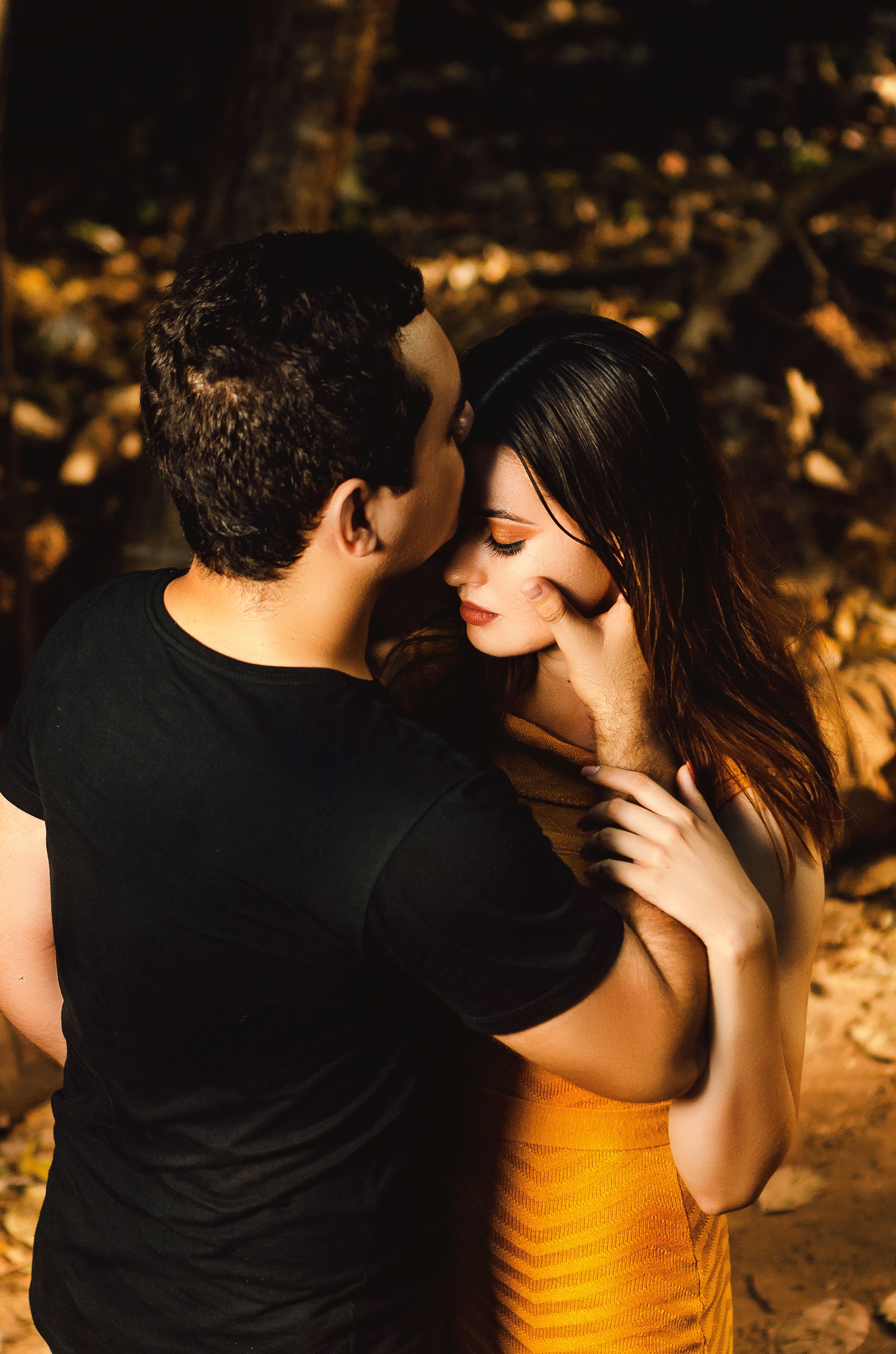 Intimate moment of a couple embracing in a sunny forest setting.