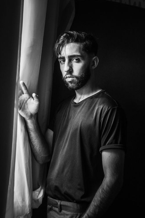 Free Black and white portrait of a bearded man standing by a window with a serious expression. Stock Photo