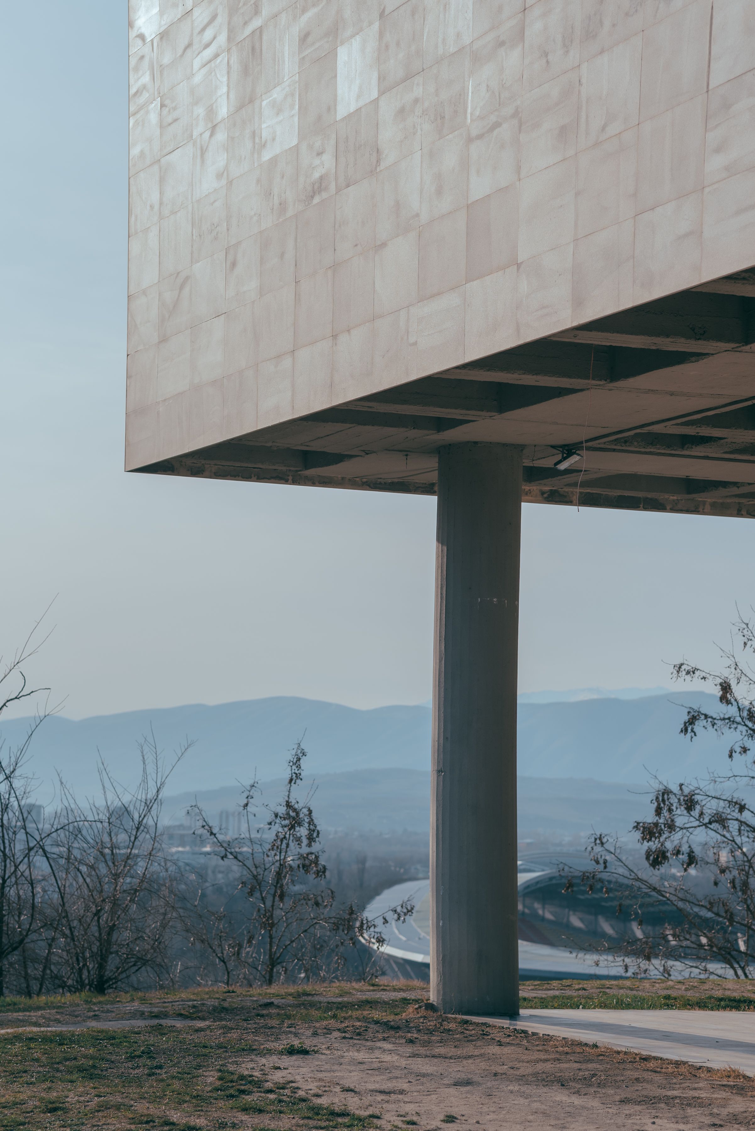 Contemporary building facade with pillar against a mountainous backdrop in Skopje, North Macedonia.