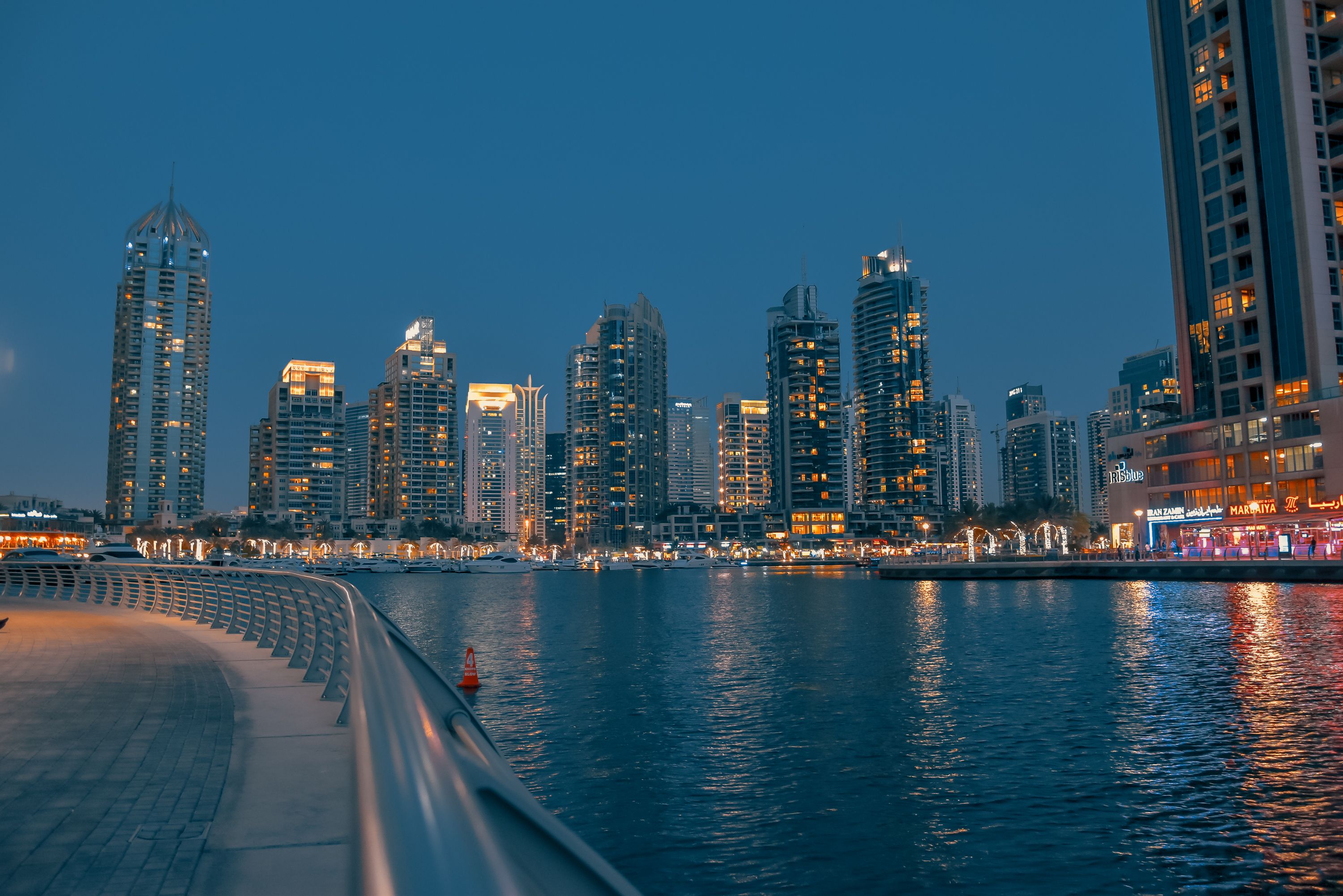 Night view of Dubai Marina Walk with illuminated towers and waterfront reflections.